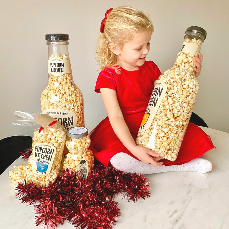 Girl holding a bottle of giant popcorn and with other popcorn products around her