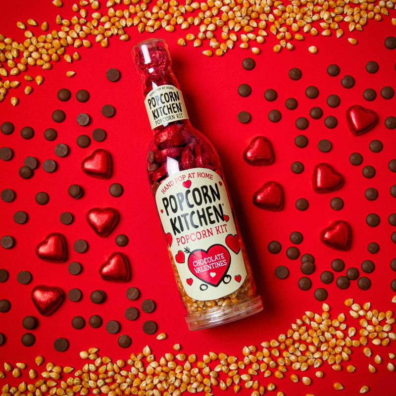 bottle of pop at home chocolate valentines surrounded by a a pattern of popcorn kernels, chocolate buttons and red foil wrapped chocolate hearts